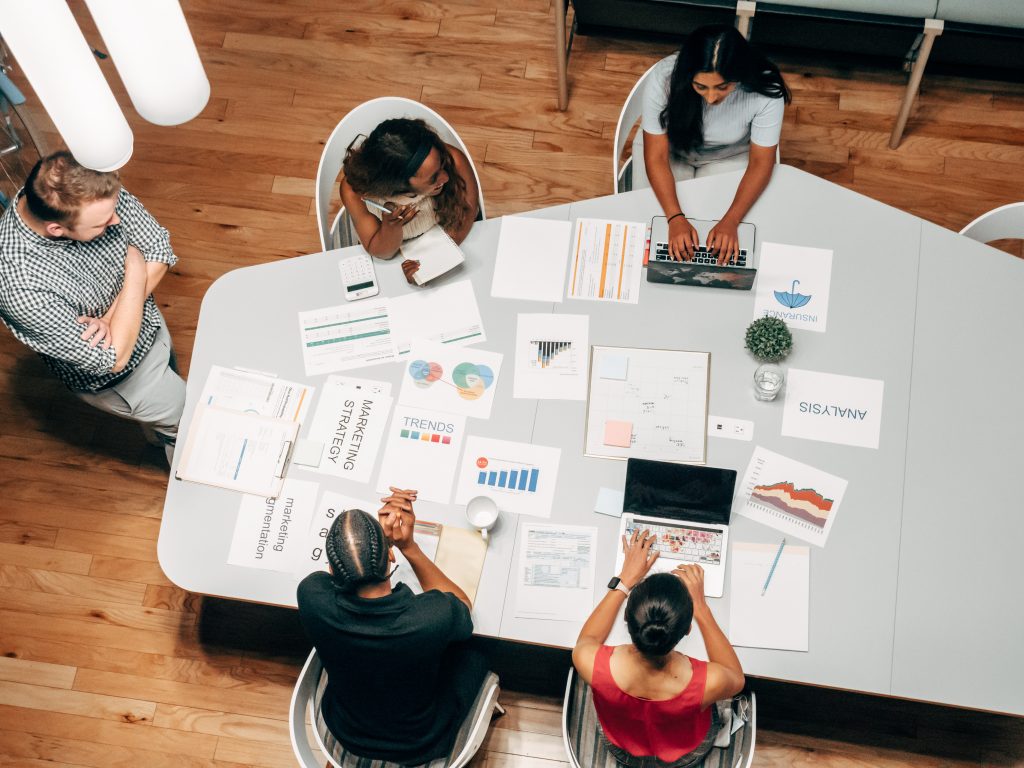 Pessoas numa mesa em reunião de trabalho com documentos de marketing, traçando plano ou estratégia